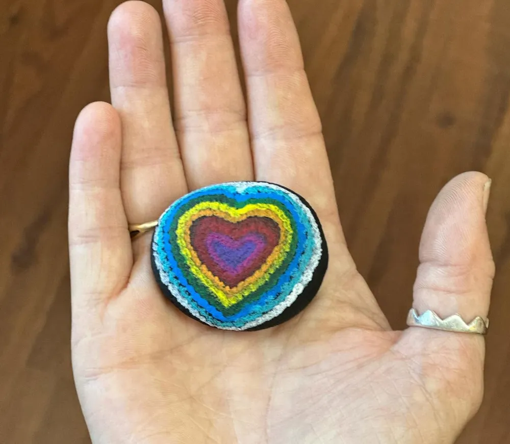A painted rainbow heart stone resting in an open palm